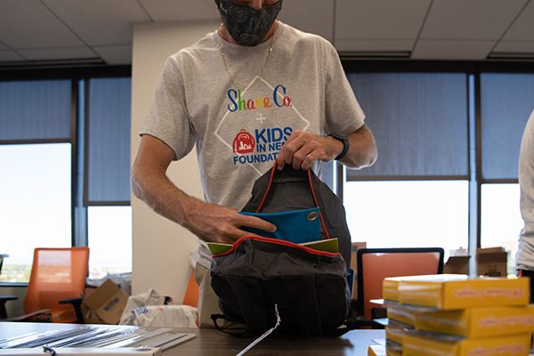 Mobile Image Of A Shane Co. employee packing a backpack with school supplies