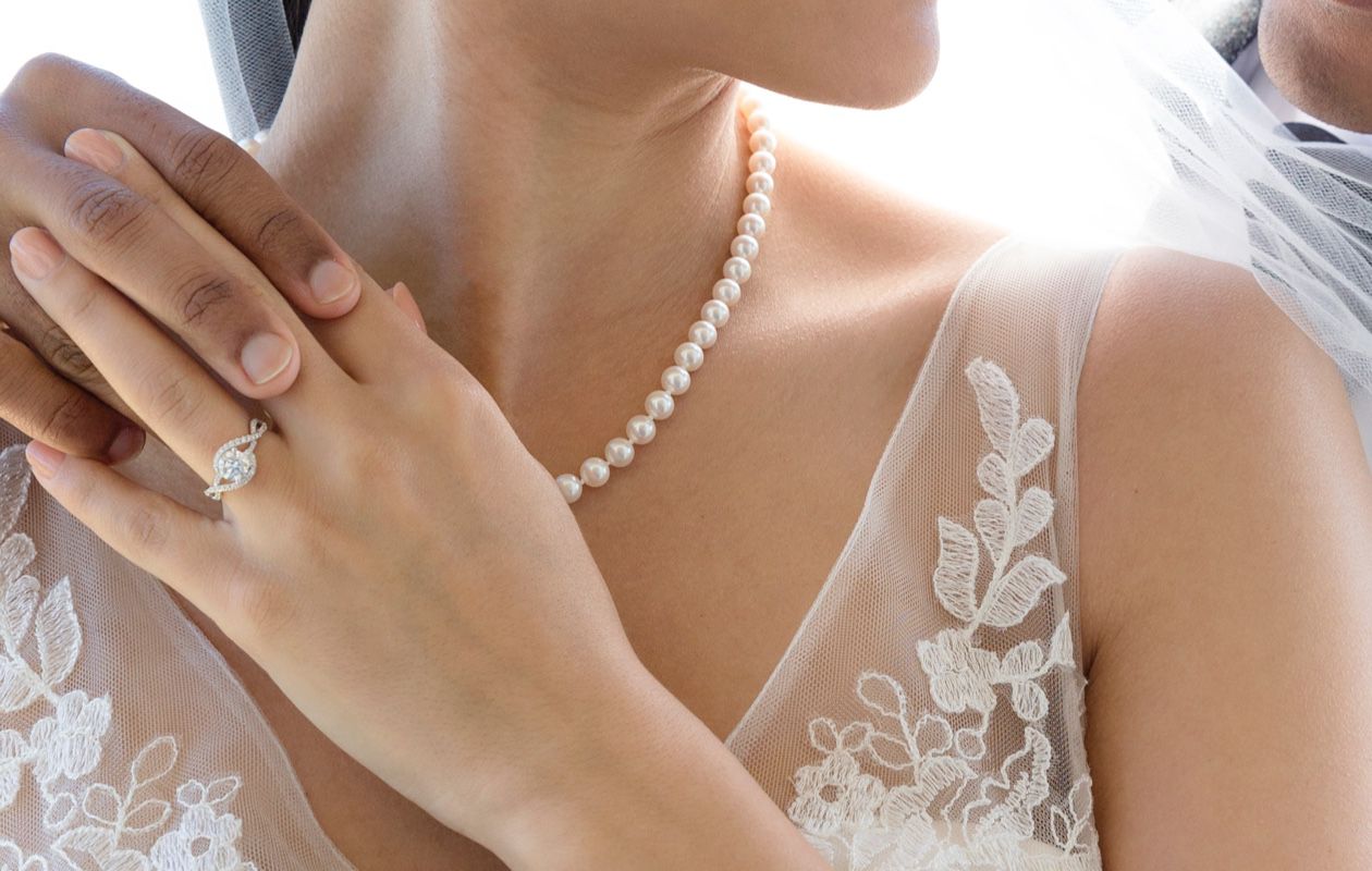 A bride wearing her engagement ring and a pearl strand necklace