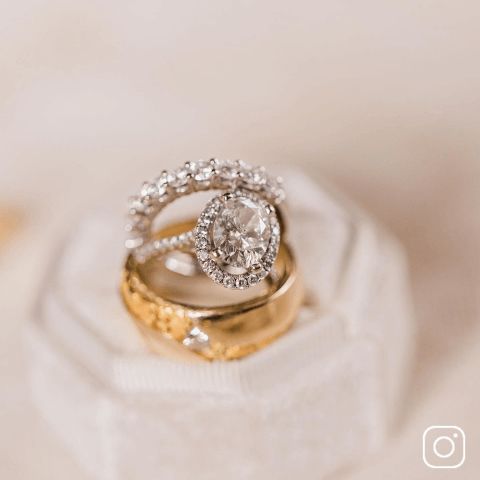 A woman's engagement ring and wedding band stack on top of a men's wedding band