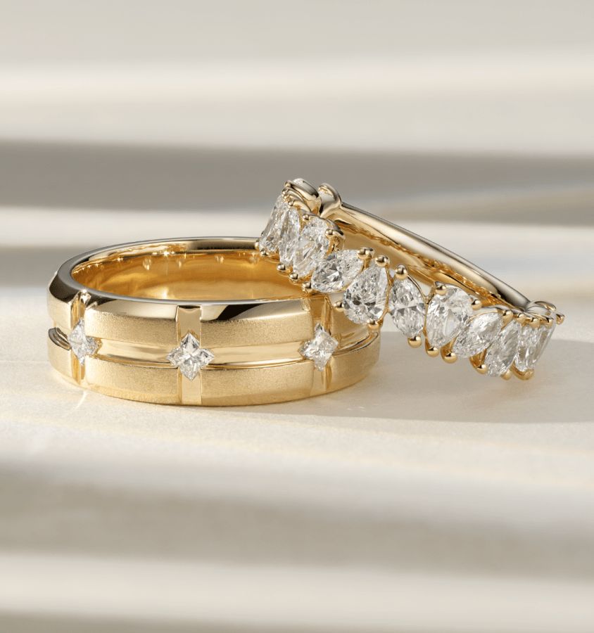 A man's diamond wedding band with a woman's diamond wedding band resting on top of it
