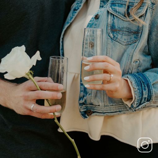 A bride and groom holding champagne glasses showing their engagement rings