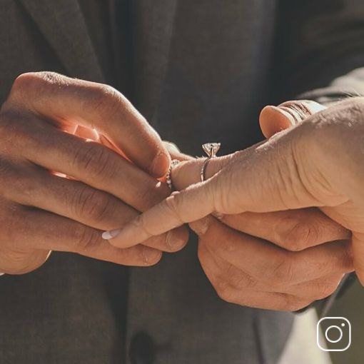 A groom placing an engagement ring on his bride's finger