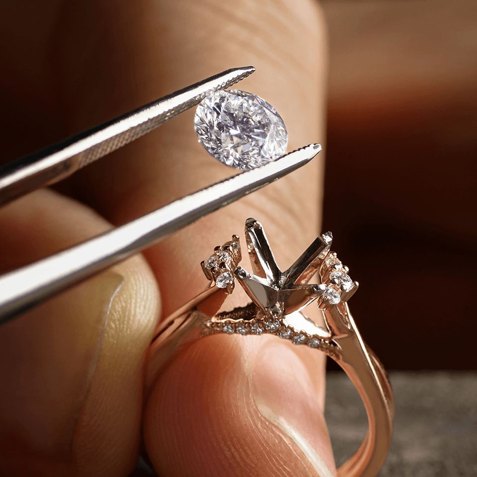 A close up of a jeweler setting a diamond center stone into a diamond engagement ring setting