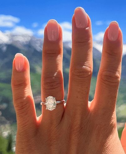 A woman's hand showing a diamond engagement ring with mountains in the background