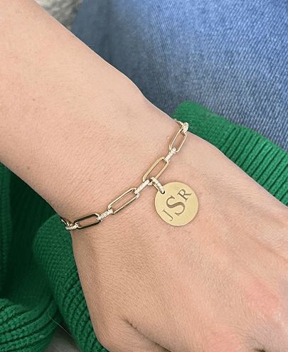 A woman's wrist with an engraved disc charm on a paperclip bracelet