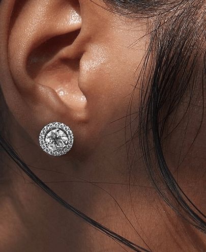 A close up of a woman's ear wearing a solitaire stud with a diamond earring jacket surrounding it