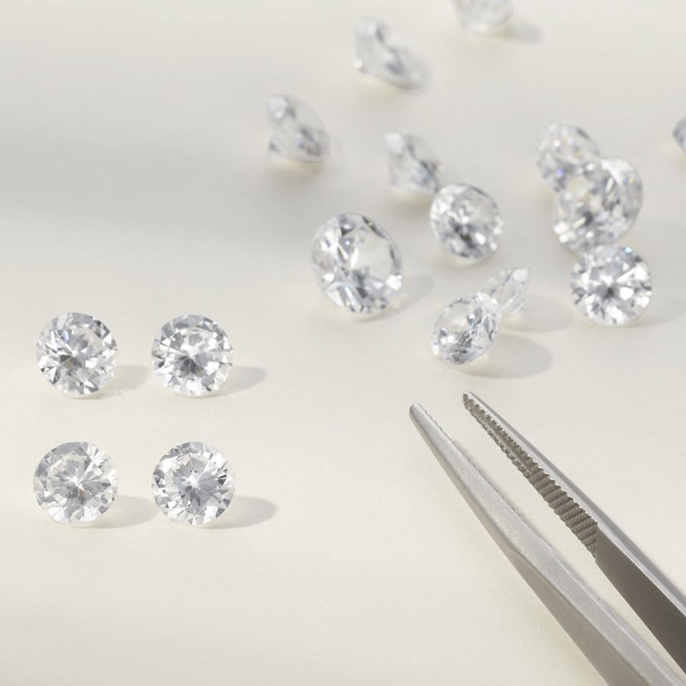 A pair of tweezers surrounded by different sizes of loose diamonds