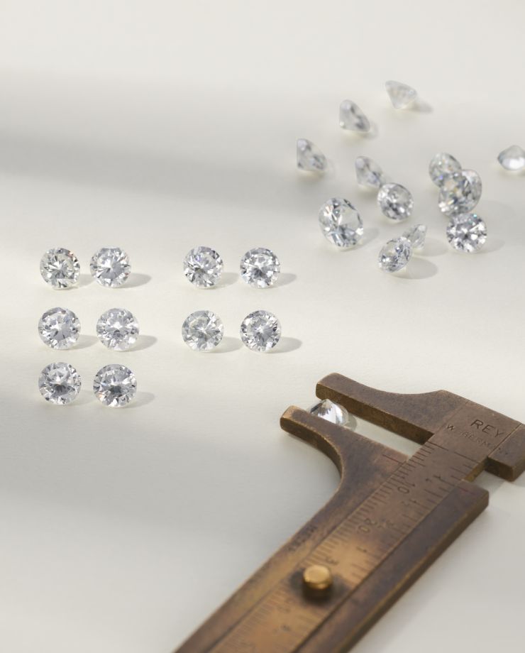 A collection of loose round diamonds next to a measuring caliper