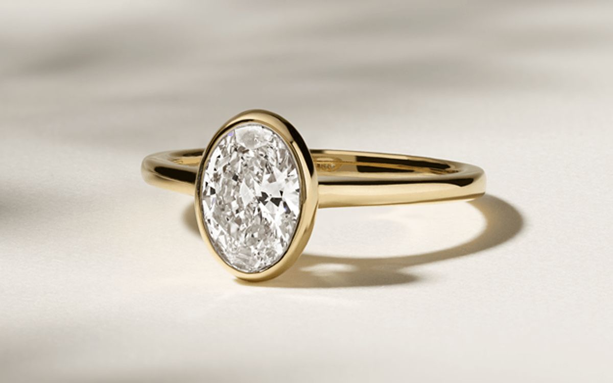 A bezel set diamond engagement ring with an oval center stone
