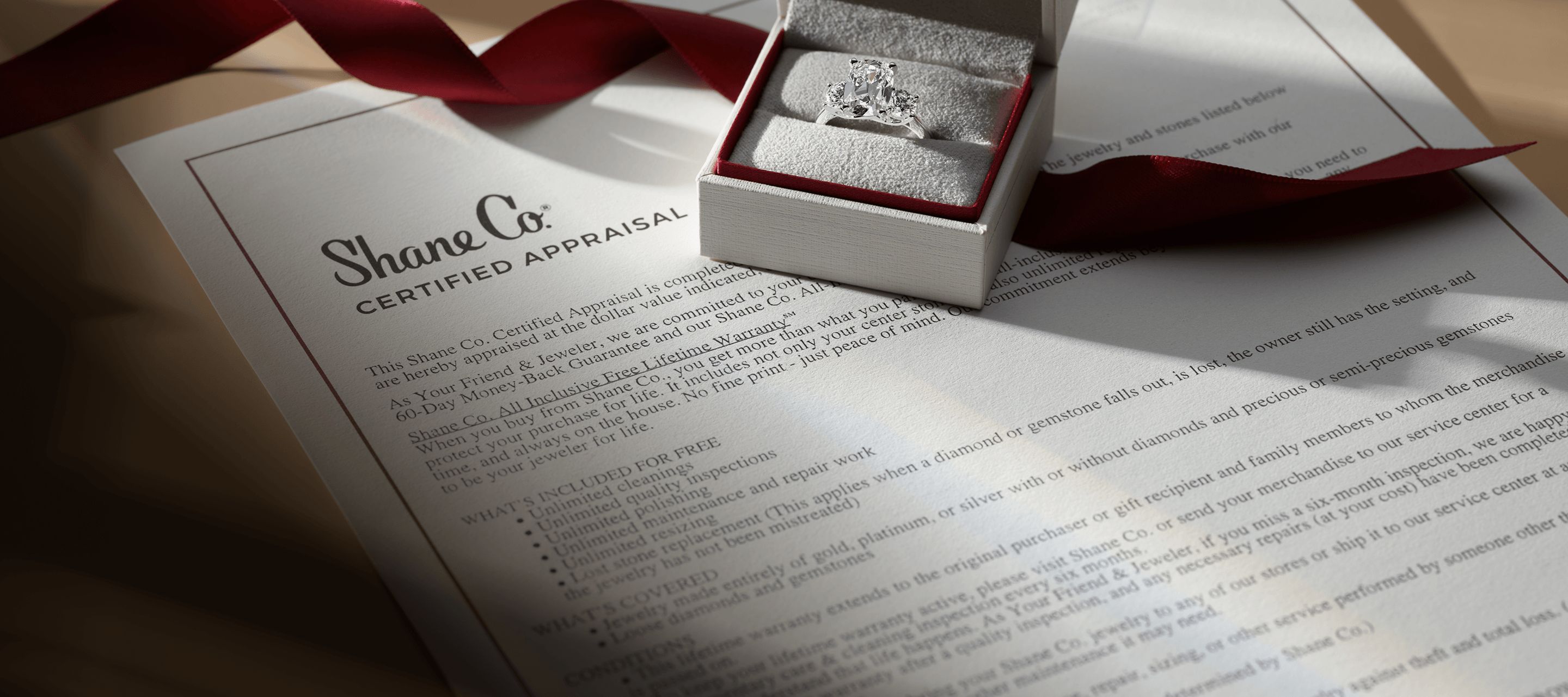 A jewelry box holding a diamond engagement ring sitting on top of a Shane Co. certified appraisal