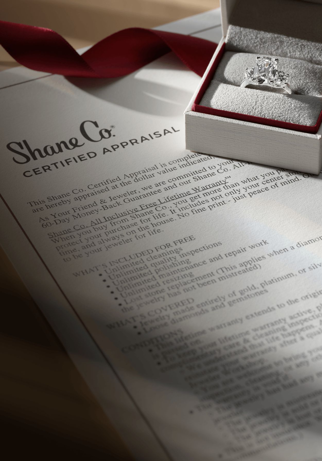 A jewelry box holding a diamond engagement ring sitting on top of a Shane Co. certified appraisal