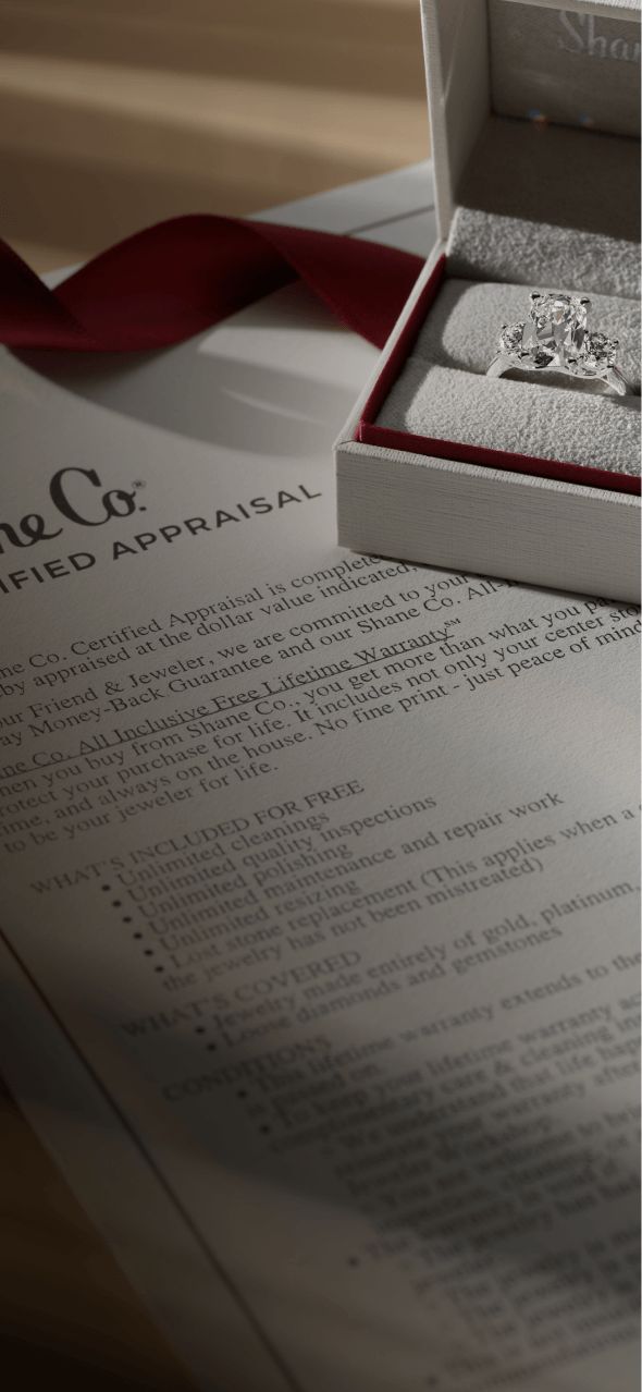 A jewelry box holding a diamond engagement ring sitting on top of a Shane Co. certified appraisal