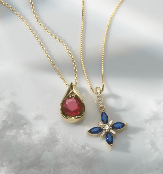 A solitaire gemstone pendant and a gemstone and diamond flower pendant surrounded by snow.