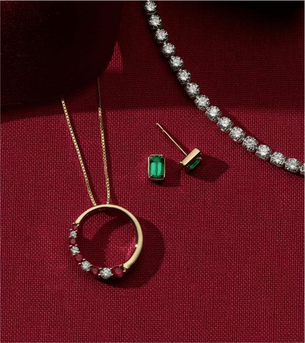 A diamond tennis bracelets next to a pair of gemstone solitaire earrings and a gemstone and diamond fashion pendant.