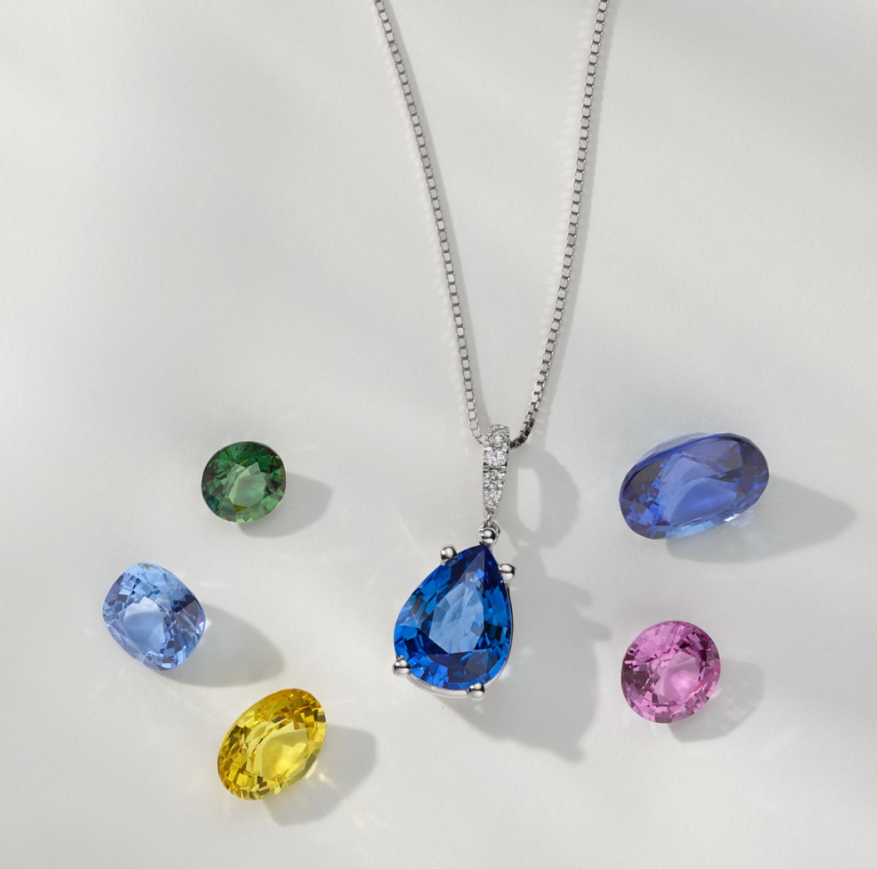 A sapphire pendant surrounded by loose colored sapphires.