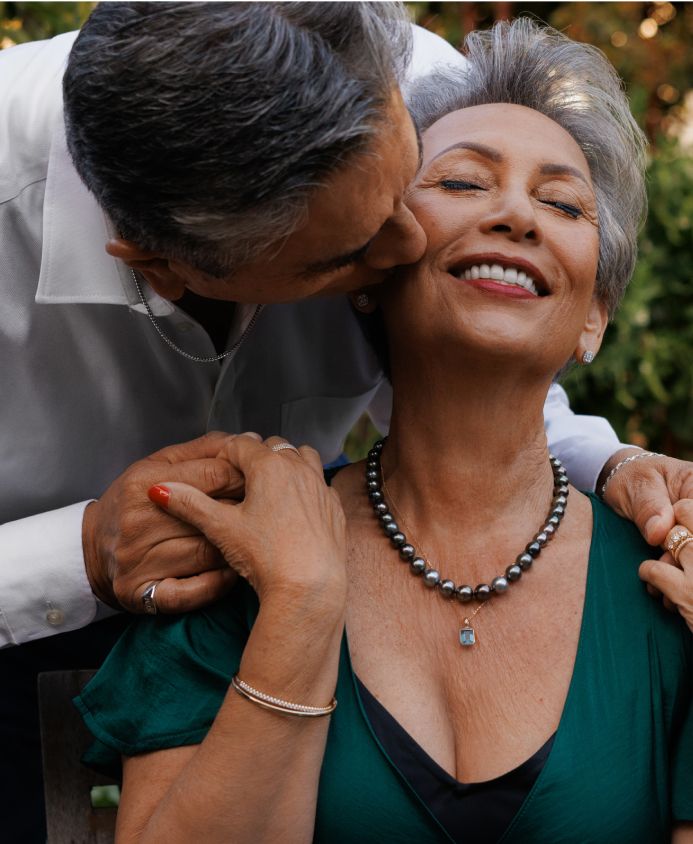 A husband kissing his wife who is wearing a tahitian pearl necklace