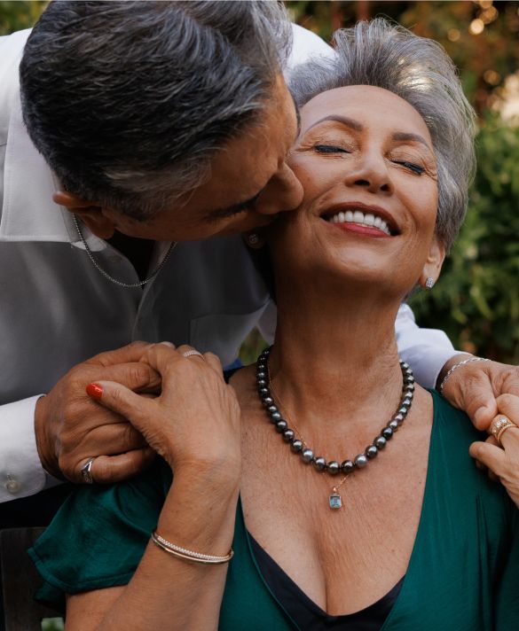 A husband kissing his wife who is wearing a tahitian pearl necklace