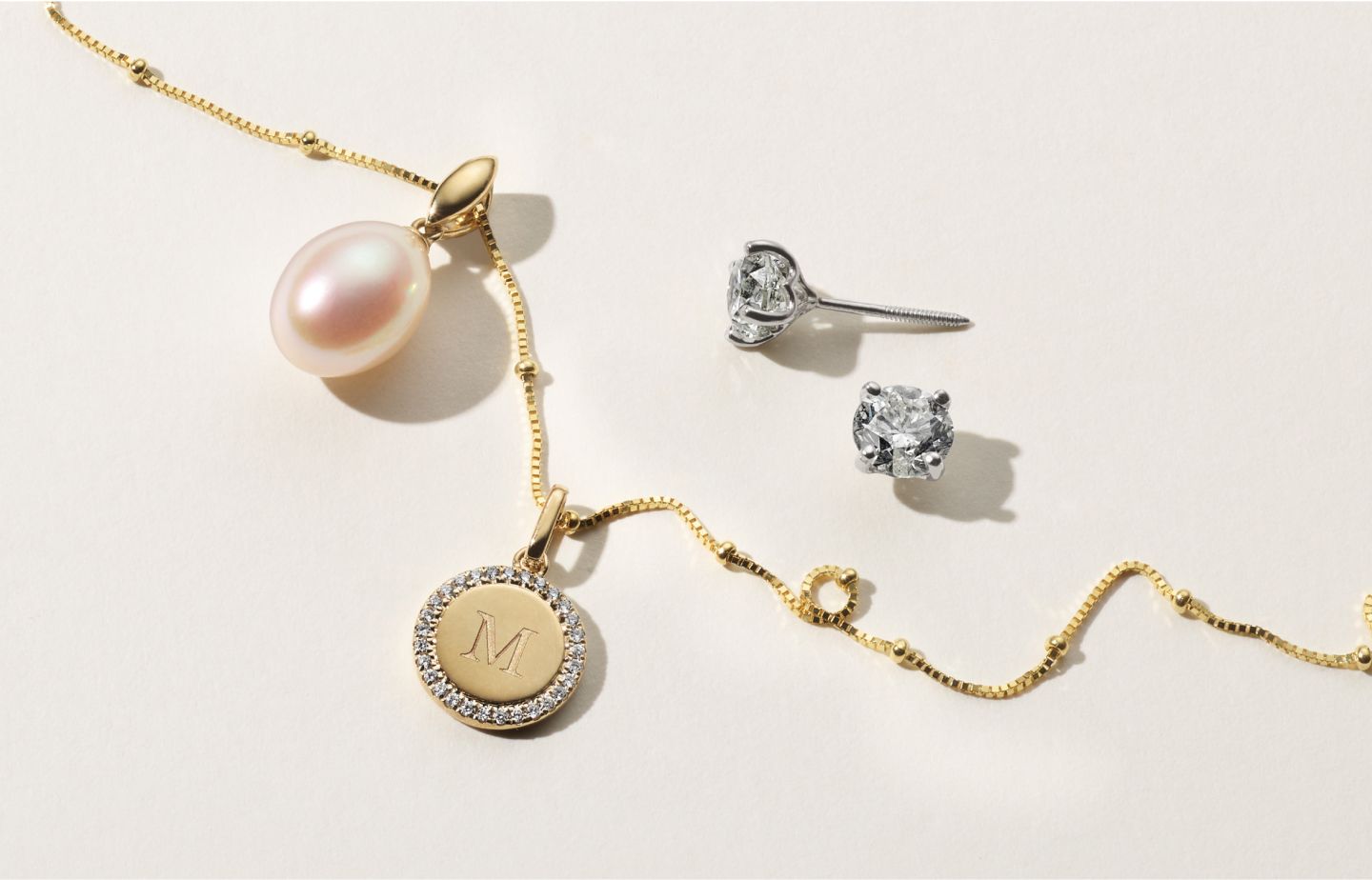 A fashion neclace with a pearl pendant and a monogrammed diamond disk charm and a pair of diamond stud earrings